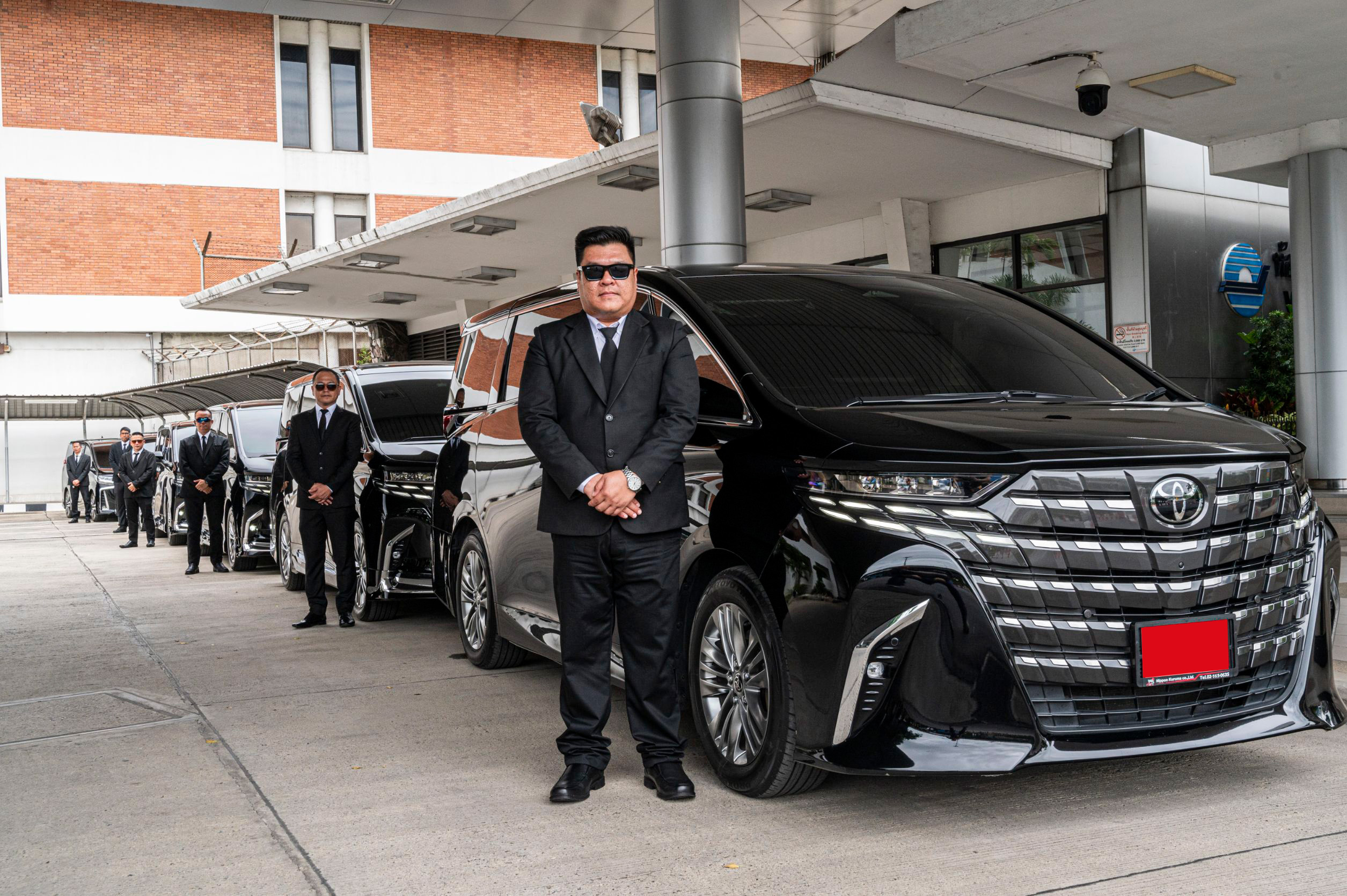 คนขับมืออาชีพยืนข้างรถ Toyota Alphard สีดำ พร้อมให้บริการเช่ารถอัลพาร์ดรับส่งสนามบิน